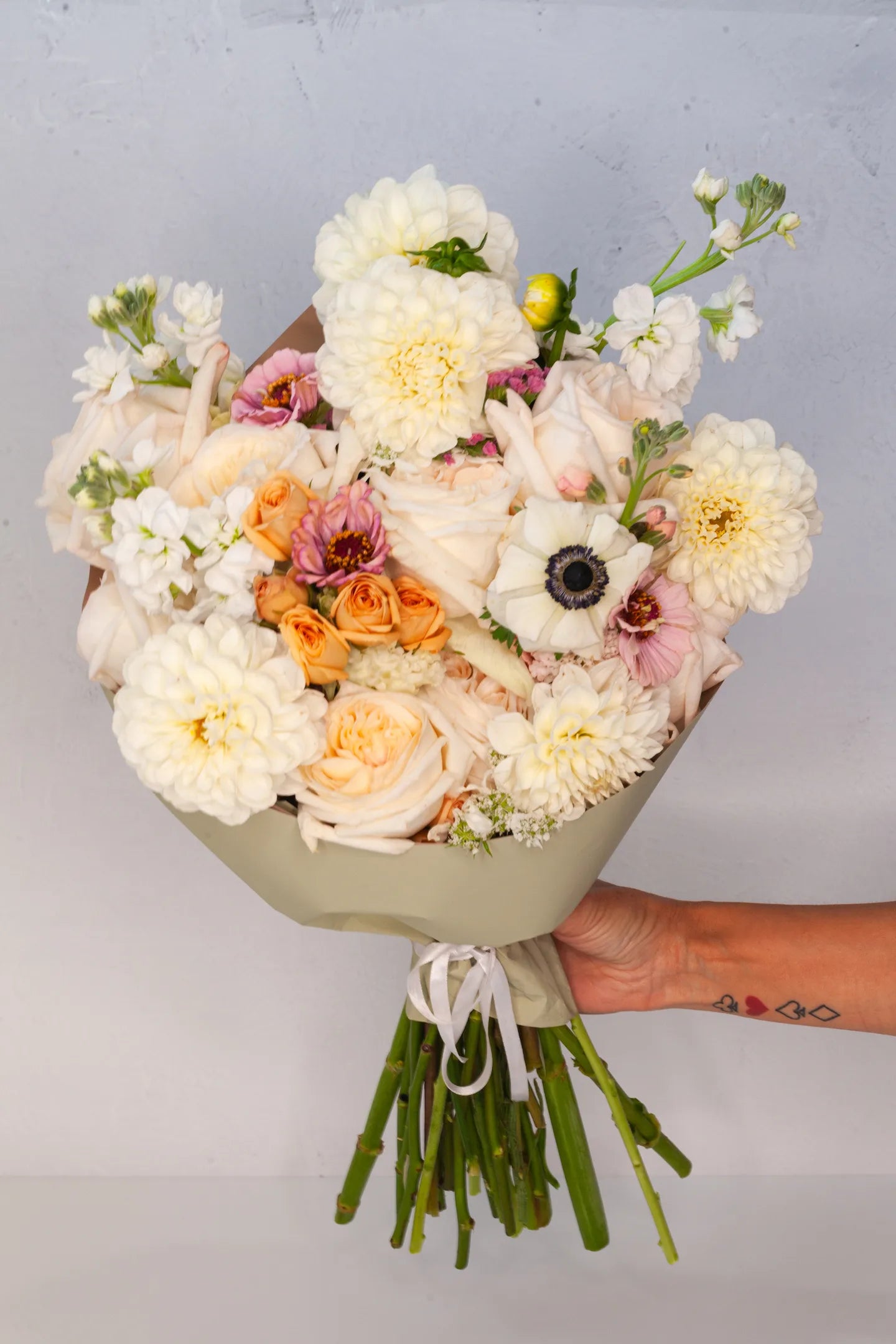 Hand holding a large wrapped bouquet with light pastel flowers.