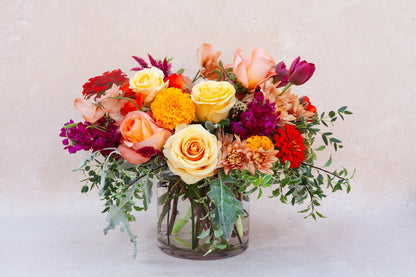 Lush garden arrangement in a glass vase with bright and colorful flowers.