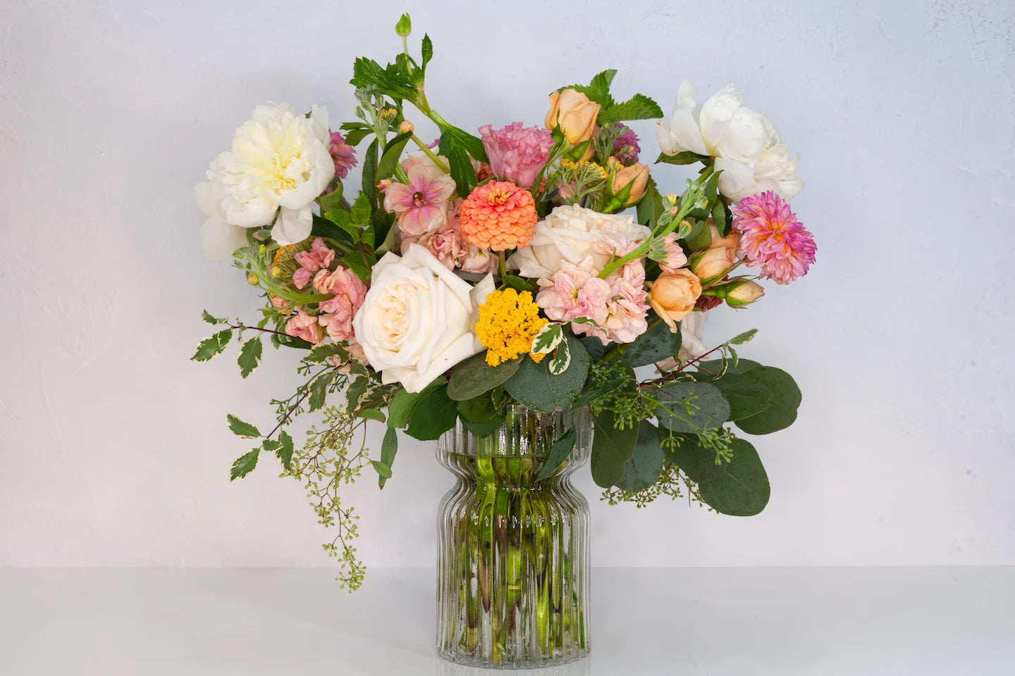 Luxe garden flower arrangement with yellow and orange tones in a glass vase.