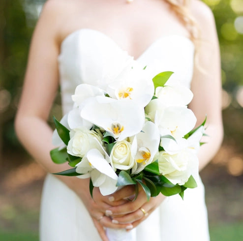 Close-up of a bride holding a white wedding bouquet with lilies.